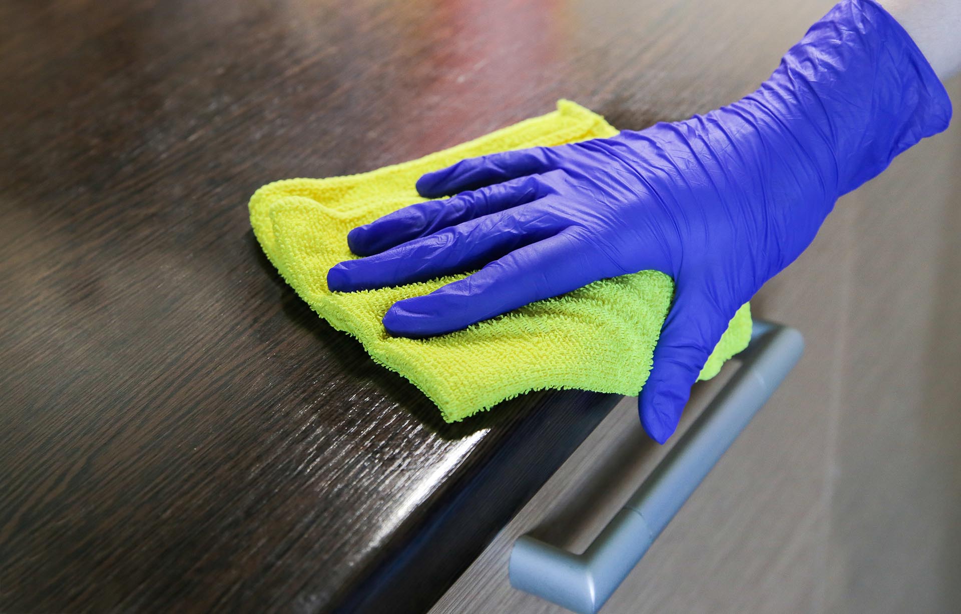 Closeup on woman's hands in blue protective rubber gloves cleaning kitchen cabinets