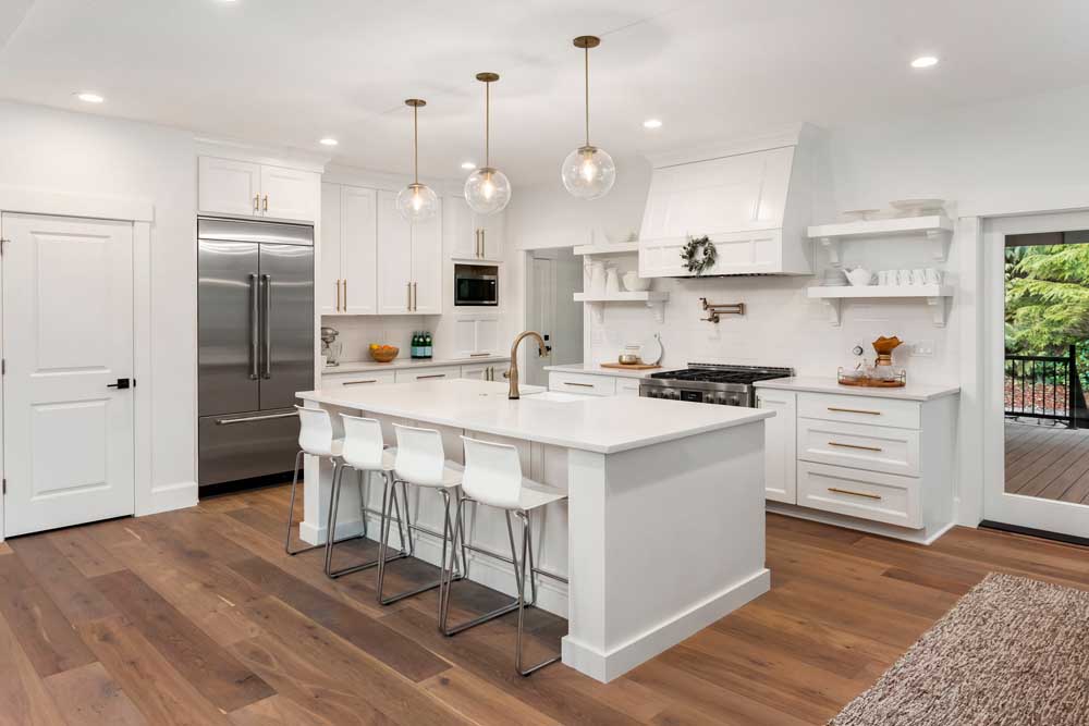 beautiful white kitchen in new luxury home with island, pendant lights, hardwood floors, and stainless steel appliances