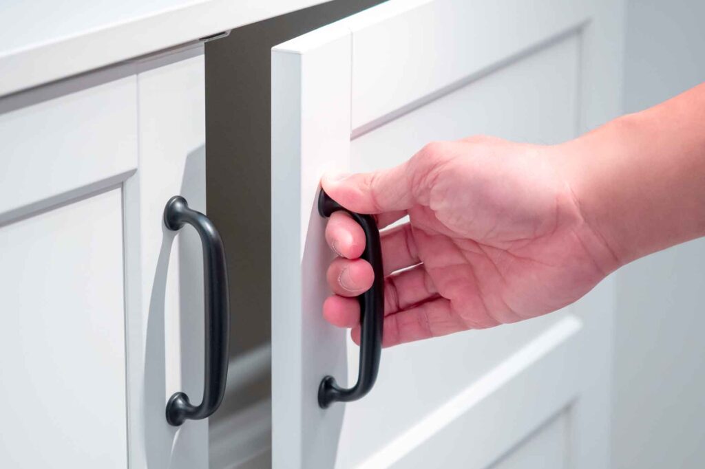 Close up of hand opening a white kitchen cabinet with black handle