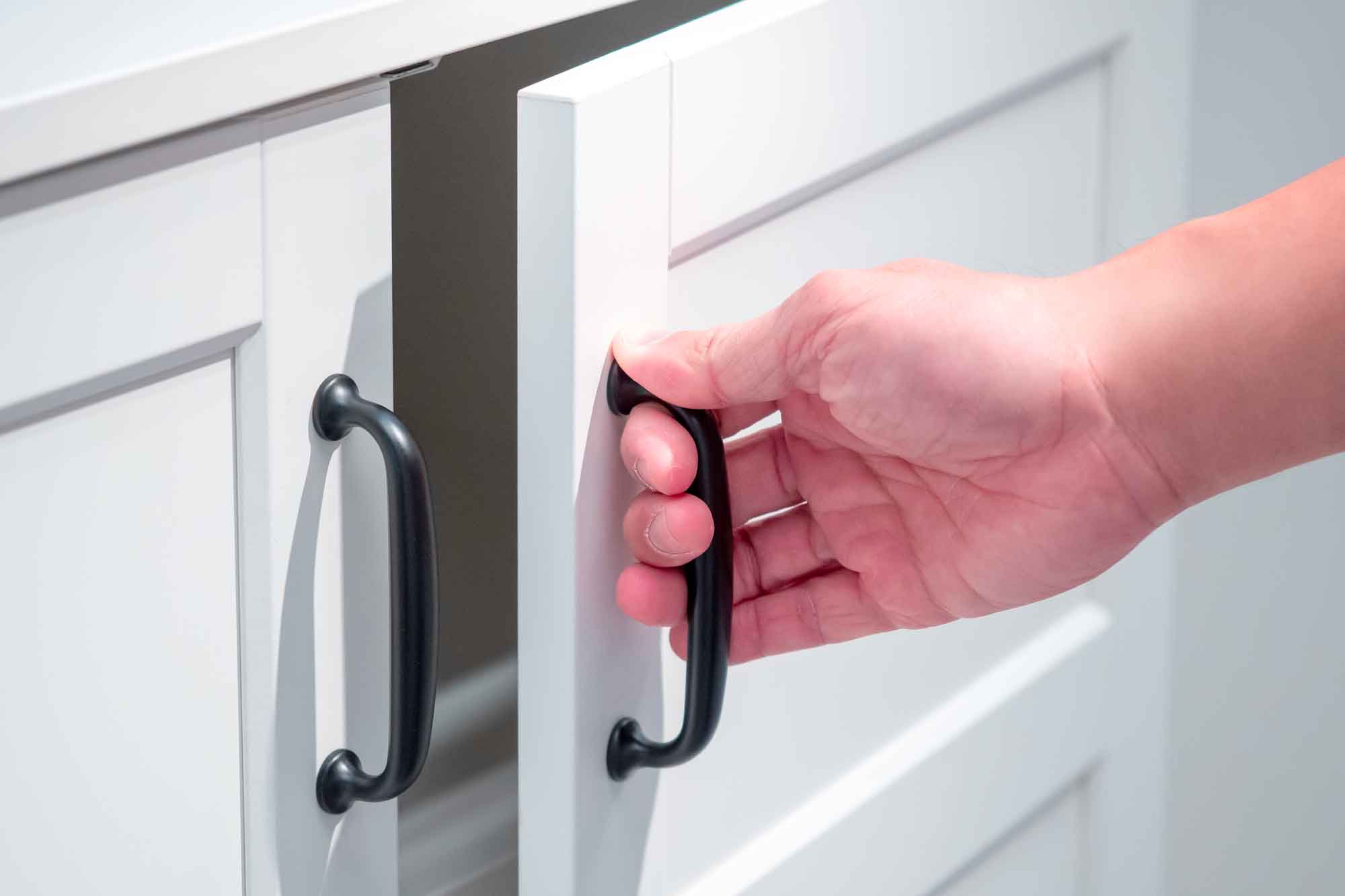 kitchen-cabinet Close up of hand opening a white kitchen cabinet with black handle